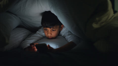 Close-Up-Of-Young-Boy-In-Bedroom-At-Home-Using-Mobile-Phone-To-Text-Message-Under-Covers-Or-Duvet-At-Night-10